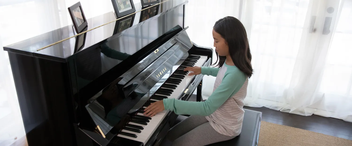 A child playing a Yamaha upright piano by a bright window